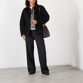 Model wearing Rohe Double-Faced Sculptural Jacket in black with wide-leg trousers, carrying a dark brown bag.