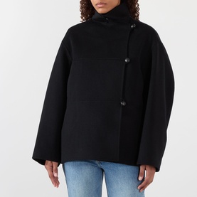 Model wearing Rohe Double-Faced Asymmetric Jacket in black with funnel neck, off-centre buttons and wide sleeves, styled with blue jeans.