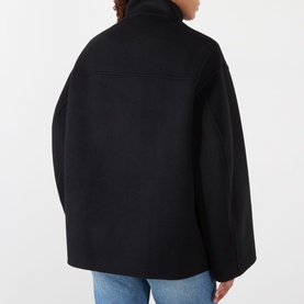 Model wearing Rohe Double-Faced Asymmetric Jacket in black, rear view showing wide-cut sleeves and wool-cashmere blend finish, styled with blue jeans.