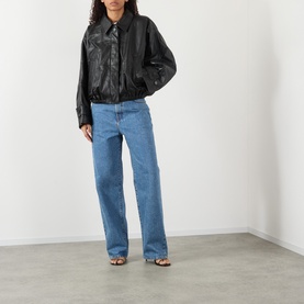 Model wearing Rohe black leather bomber jacket with collar, styled with blue straight-leg jeans and strappy heeled sandals.