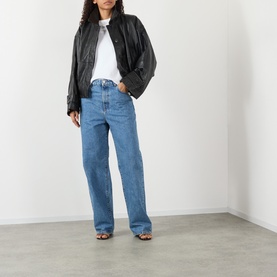 Model wearing Rohe black leather bomber jacket, styled with white T-shirt, blue wide-leg jeans and brown strappy heeled sandals.