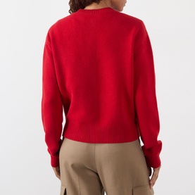 Model wearing Rohe Classic Knit Cardigan in red, back view, round neckline, dropped shoulders, styled with beige trousers.