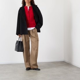 Model wearing Rohe Classic Knit Cardigan in red, styled with black oversized jacket, tan wide-leg trousers, and carrying a black tote bag.