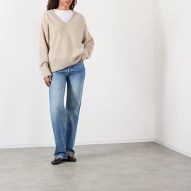 Model wearing Rohe Classic Moulin&eacute; Sweater in Oat Melange with V-neck and dropped shoulders, styled with blue wide-leg jeans and black flats.