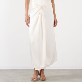 Model wearing Rohe ivory maxi skirt with twisted front knot detail, styled with tan strappy flat sandals.