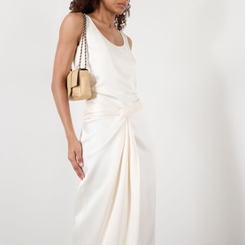 Model wearing Rohe ivory draped midi skirt with knotted front detail, styled with white vest top and beige chain-strap bag.