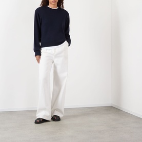 Model wearing Rohe Statement Knit Sweater in navy with crew neck and ribbed trims, styled with wide-leg white trousers and dark loafers.