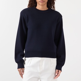 Model wearing Rohe Statement Knit Sweater in navy with crew neck, shoulder pads, and ribbed trims, styled with white trousers.
