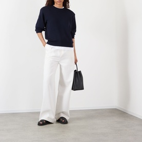 Model wearing Rohe Statement Knit Sweater in navy with crew neck and shoulder pads, styled with wide-leg white trousers and black loafers.