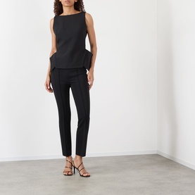 Model wearing Rohe Deconstructed Peplum Top in black with boat neckline and peplum hem, styled with black slim trousers and strappy heels