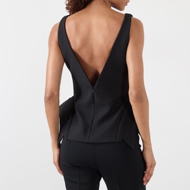 Model wearing Rohe Deconstructed Peplum Top in black, showing deep V-back with zip detail, peplum hemline, paired with black trousers