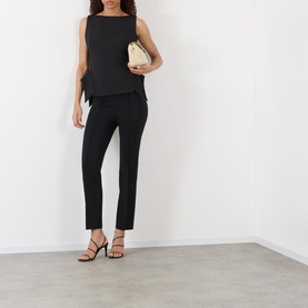 Model wearing Rohe Deconstructed Peplum Top in black with matching black trousers, carrying a small cream clutch, styled with black strappy heels.