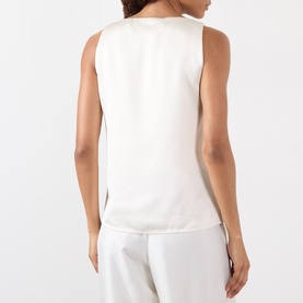 Model wearing Rohe Solid Fluid Top in ivory, back view, sleeveless satin finish with straight hemline, styled with white trousers.