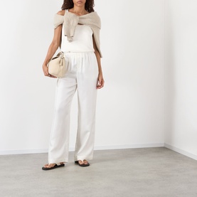 Model wearing Rohe Solid Fluid Top in ivory, styled with wide-leg white trousers, a draped scarf, and black sandals, carrying a cream bag.