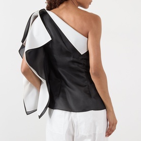 Model wearing Rohe black silk one-shoulder top with contrasting white ruffle drape detail, styled with white trousers. Back view.