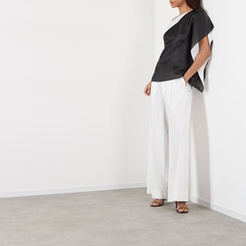 Model wearing Rohe black silk asymmetric top with wide-leg white trousers and tan strappy heeled sandals.