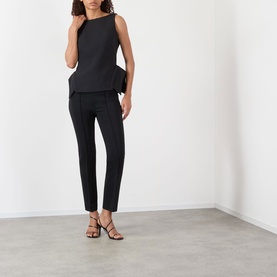 Model wearing Rohe black slim-leg trousers, styled with a black sleeveless top and strappy heeled sandals.