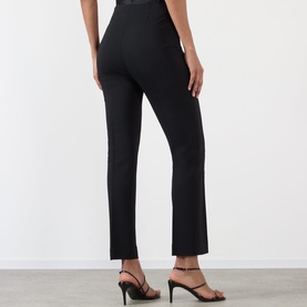 Model wearing Rohe black slim-leg trousers in viscose-elastane blend, shown from behind, styled with black strappy heeled sandals.