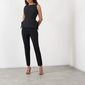 Model wearing Rohe black slim-leg trousers in viscose blend, styled with a black sleeveless peplum top and strappy heeled sandals.