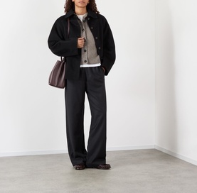 Model wearing Rohe Wide Leg Trousers in Anthracite Melane. Styled with black jacket, grey cardigan and burgundy shoulder bag.