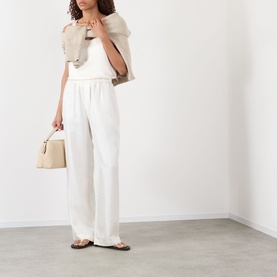 Model wearing Rohe cream silk wide-leg trousers with a white top and beige jacket, carrying a structured handbag, wearing flat sandals