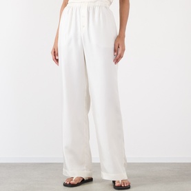 Model wearing Rohe cream silk wide-leg trousers with elasticated waist, styled with black slide sandals