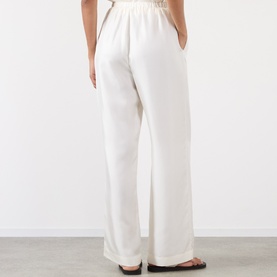 Model wearing Rohe cream silk wide-leg trousers, rear view, elasticated waistband, side pockets visible