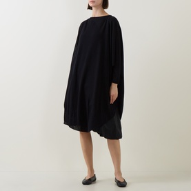 Model wearing Sarah Pacini Knitted Oversized Tunic Dress in black, midi length with asymmetric hem and boat neck, styled with black flat shoes.