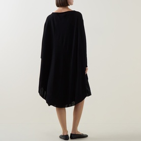Model wearing Sarah Pacini Knitted Oversized Tunic Dress in black, midi length with asymmetric hem, shown from behind with flat mules.