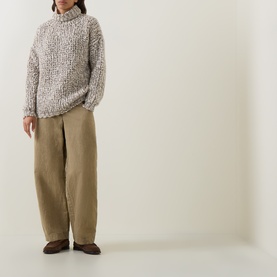 Model wearing Sarah Pacini beige chunky turtleneck knit, styled with wide-leg khaki trousers and dark loafers.