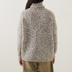 Model wearing Sarah Pacini beige chunky knit turtleneck sweater, back view, styled with khaki trousers