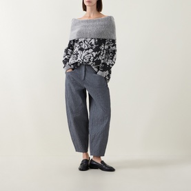 Model wearing Sarah Pacini black floral jacquard knit off-shoulder sweater, styled with grey tapered trousers and black loafers.