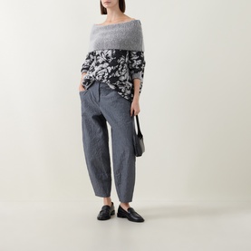Model wearing Sarah Pacini black floral knit top with grey tapered trousers and black loafers, carrying a black bag.