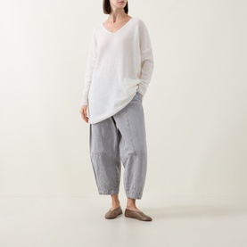 Model wearing Sarah Pacini cream oversized V-neck knit top with asymmetric hem, styled with grey striped cropped trousers and taupe flat mules