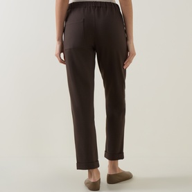 Model wearing Sarah Pacini brown trousers with elasticated waistband and cuffed hem, styled with beige flat shoes.