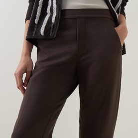 Model wearing Sarah Pacini brown trousers with front seam detail, styled with a monochrome fringed jacket.