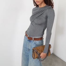 Model carrying Stella McCartney Falabella Mini Crossbody Bag in tan with silver-tone chain trim, styled with grey twist-front top and light-wash