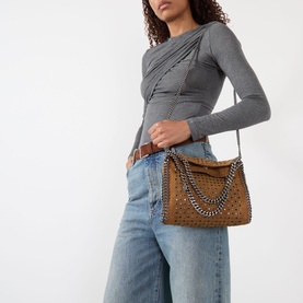 Model carrying Stella McCartney Falabella Mini Crossbody Bag in tan with silver-tone curb-chain trim and perforated detail, styled with grey top and