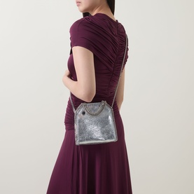 Model carrying Stella McCartney Falabella Mini Crossbody Bag in silver metallic finish with silver-tone chain trim, styled with burgundy midi dress