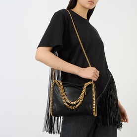 Model carrying Stella McCartney Falabella Mini Tote Bag in black with gold-tone chain trim, fringe detailing, and crossbody chain strap