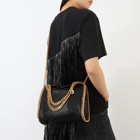 Model carrying Stella McCartney Falabella Mini Tote Bag in black with gold-tone chain strap and trim, worn crossbody over black outfit