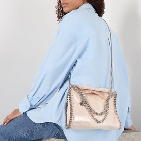 Model carrying small pale pink metallic bag with silver chain straps and trim, styled with light blue oversized shirt and jeans
