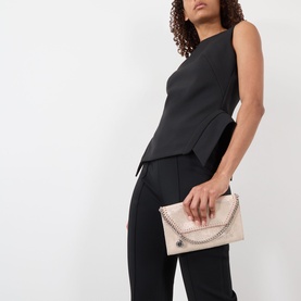 Model carrying Stella McCartney Falabella Chain Wallet in Shell Pink with silver-tone chain trim; styled with black sleeveless top and trousers.