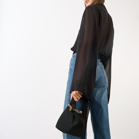 Model carrying Stella McCartney Falabella Pouch in black with gold-tone chain handle, styled with black sheer blouse and blue jeans.