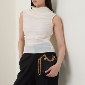 Model carrying Stella McCartney Falabella Tiny Tote Bag in black with gold-tone chain trim, worn as belt bag styling with black trousers.