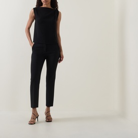 Model wearing Vince Draped Tank Top in black with asymmetric neckline, paired with slim black trousers and strappy heeled sandals.