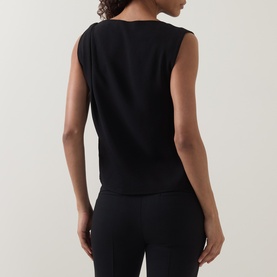 Model wearing Vince Draped Tank Top in black, rear view, showing sleeveless silhouette and curved hem, styled with black trousers