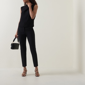 Model wearing Vince Draped Tank Top in black with asymmetric neckline, styled with black tapered trousers and strappy heels, carrying small bag.