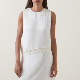 Model wearing Vince Asymmetric Lace Trim Top in cream, styled with a matching cream skirt. Sleeveless, round neckline, floral lace hem detail.