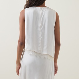 Model wearing Vince Asymmetric Lace Trim Top in cream, back view showing concealed zip, with cream satin skirt.